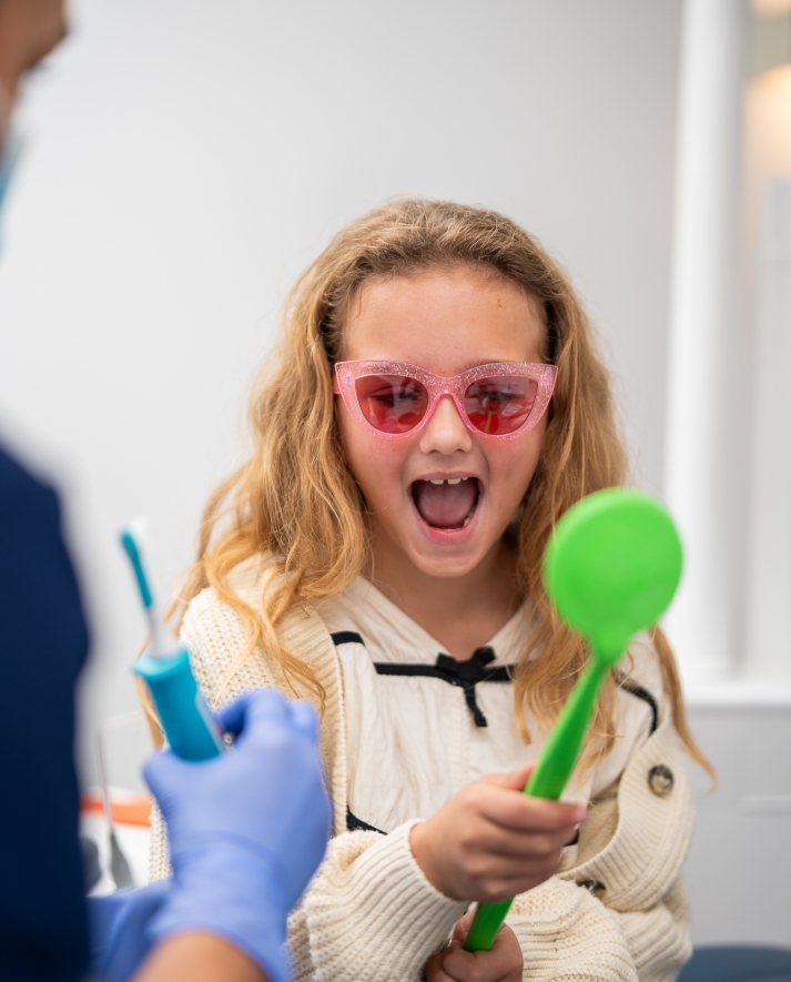 Kind met zonnebril in behandelstoel kijkend naar spiegel